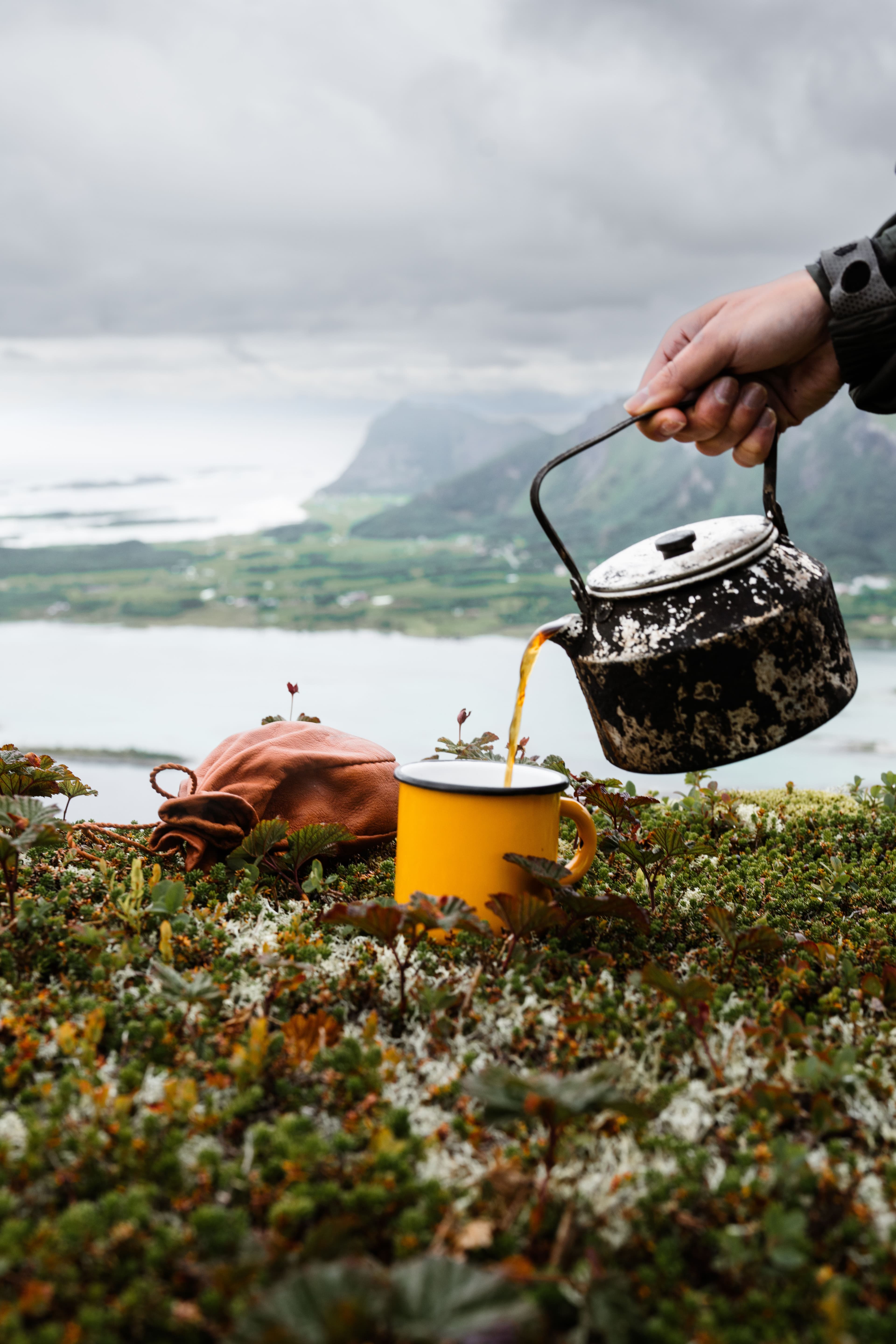 A kettle pouring coffee beside a fjord in the Norwegian mountains