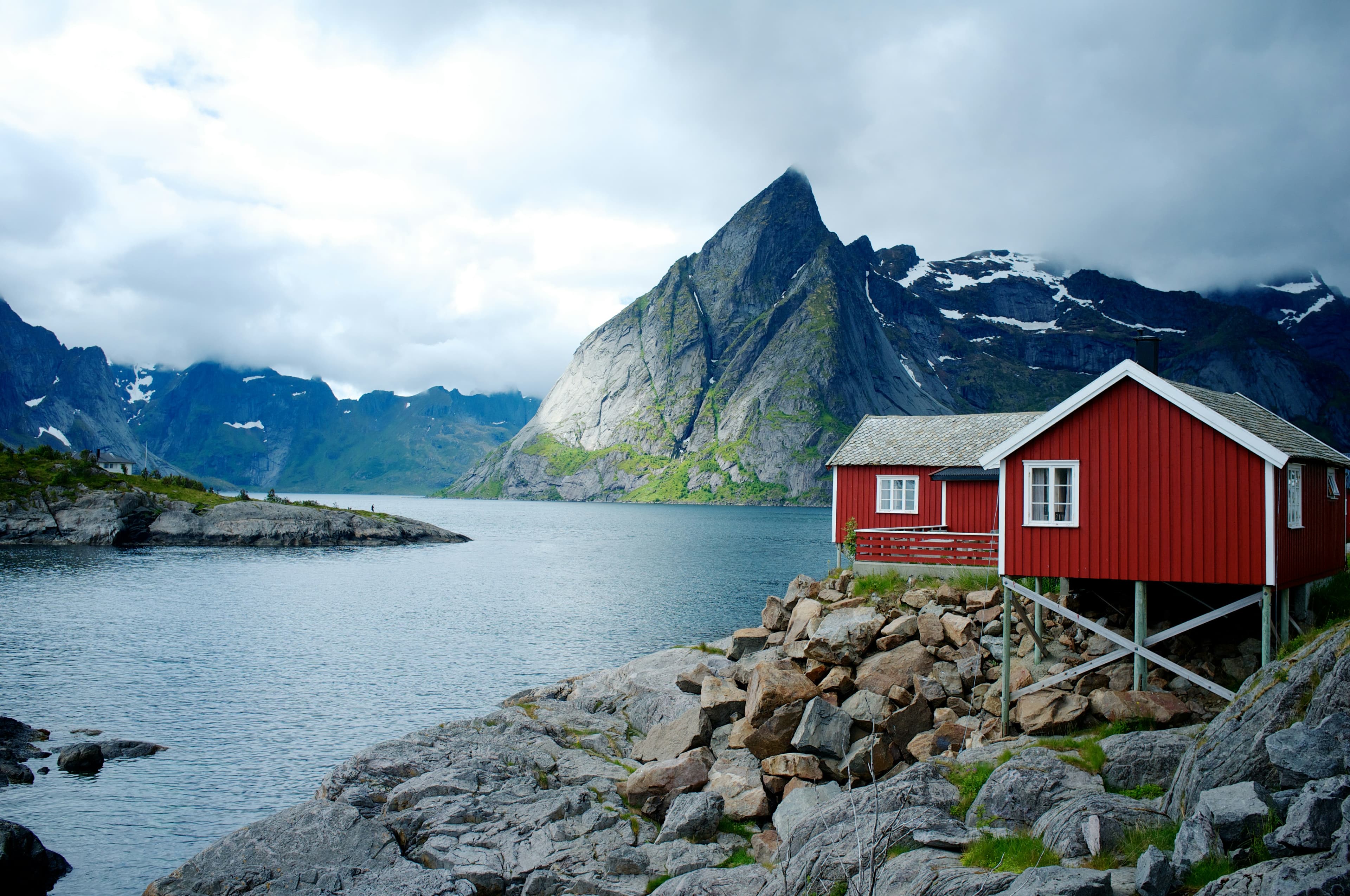 A red cabin on the fjord edge beneath a steep northern mountain