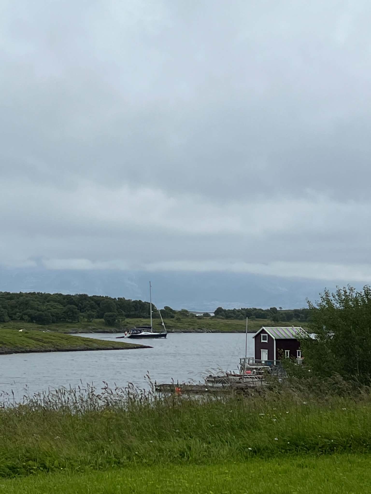 A sailboat and red boathouse beside a sheltered inlet on Herøy.