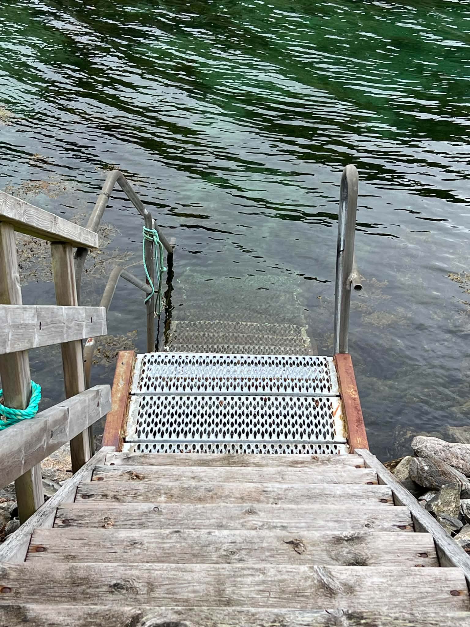 Wooden and metal bathing steps descending into clear coastal water on Herøy.