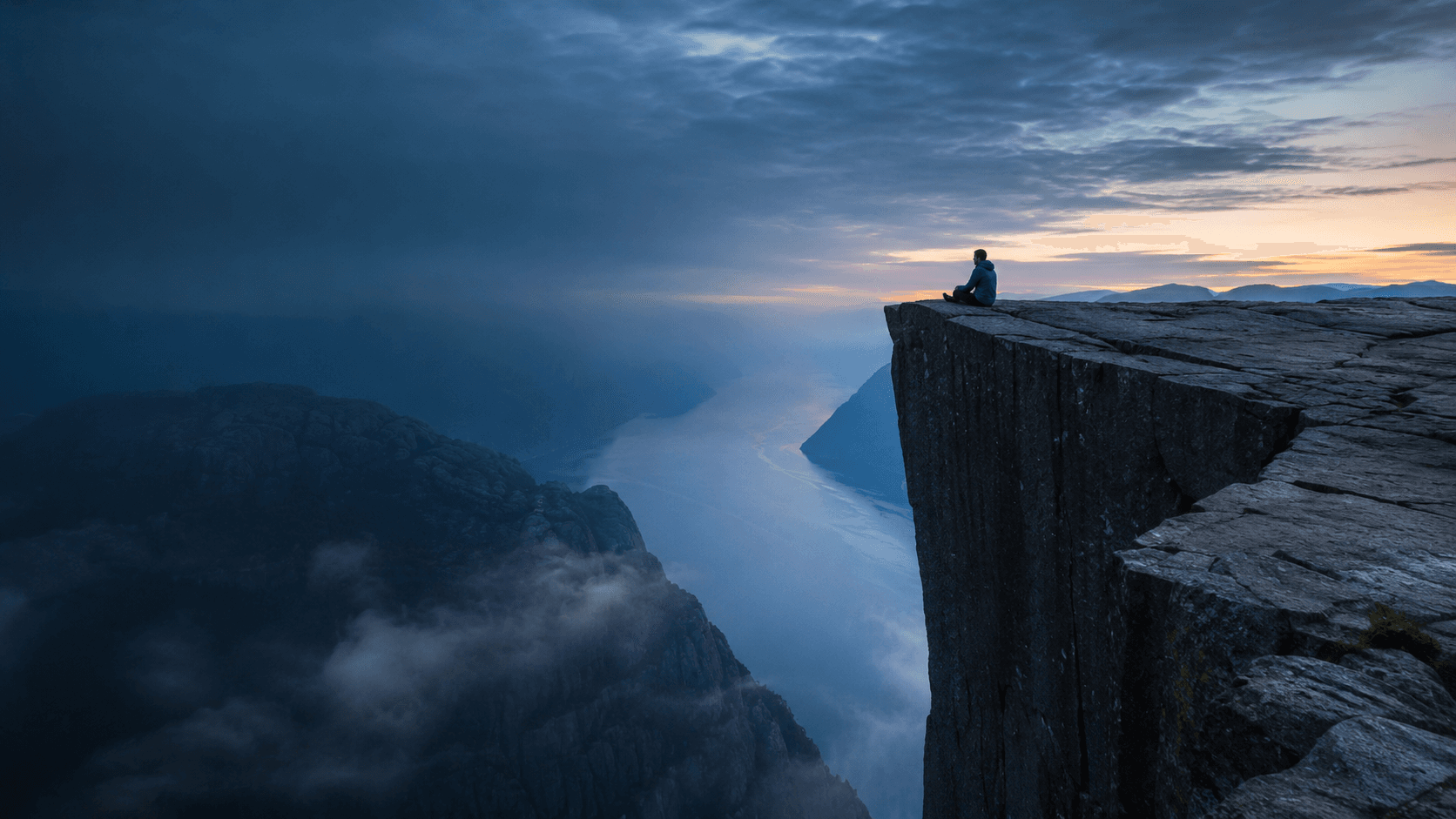 A traveler standing on Preikestolen above a Norwegian fjord