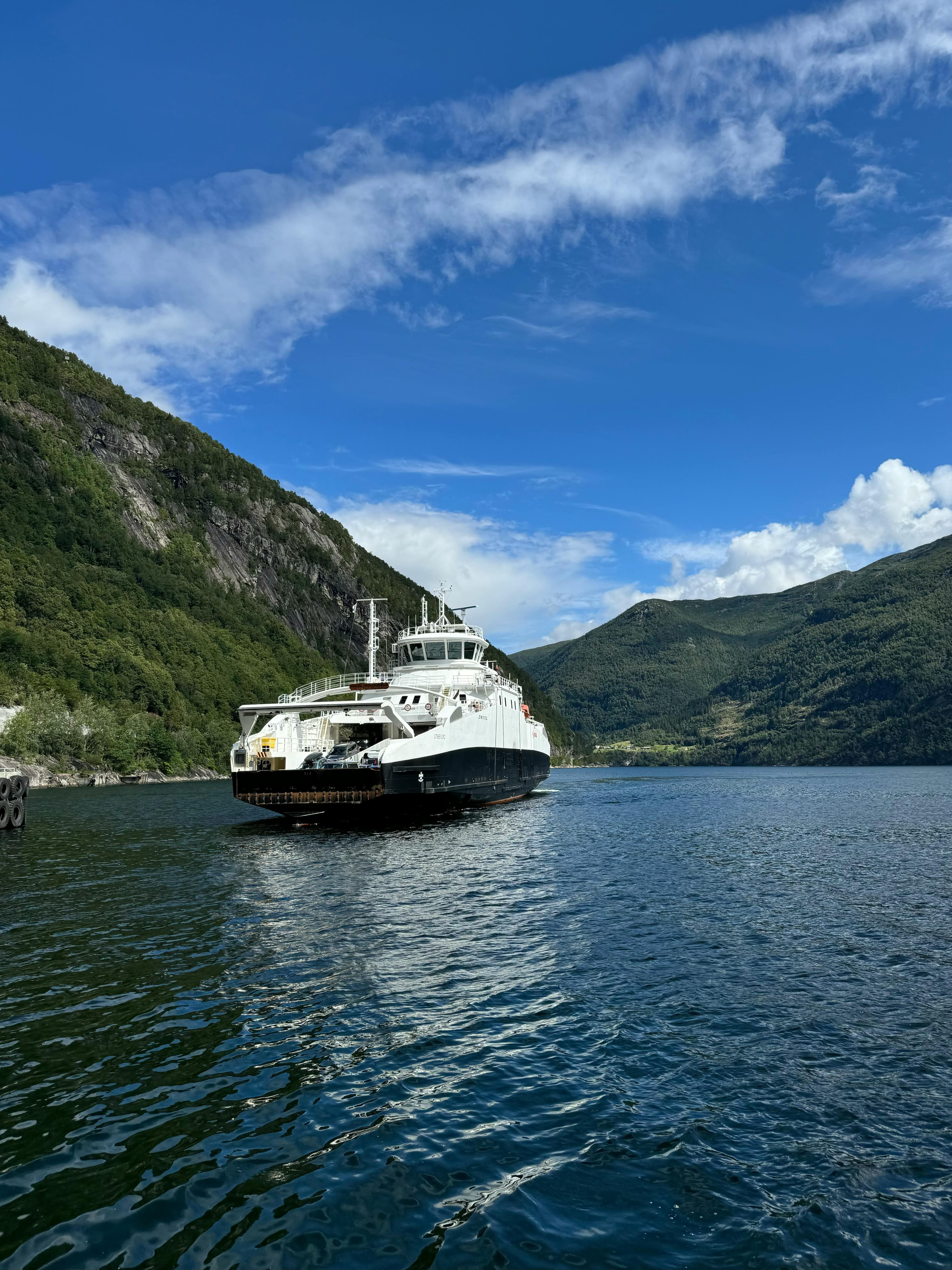 A ferry moving through a narrow Norwegian fjord between green mountains