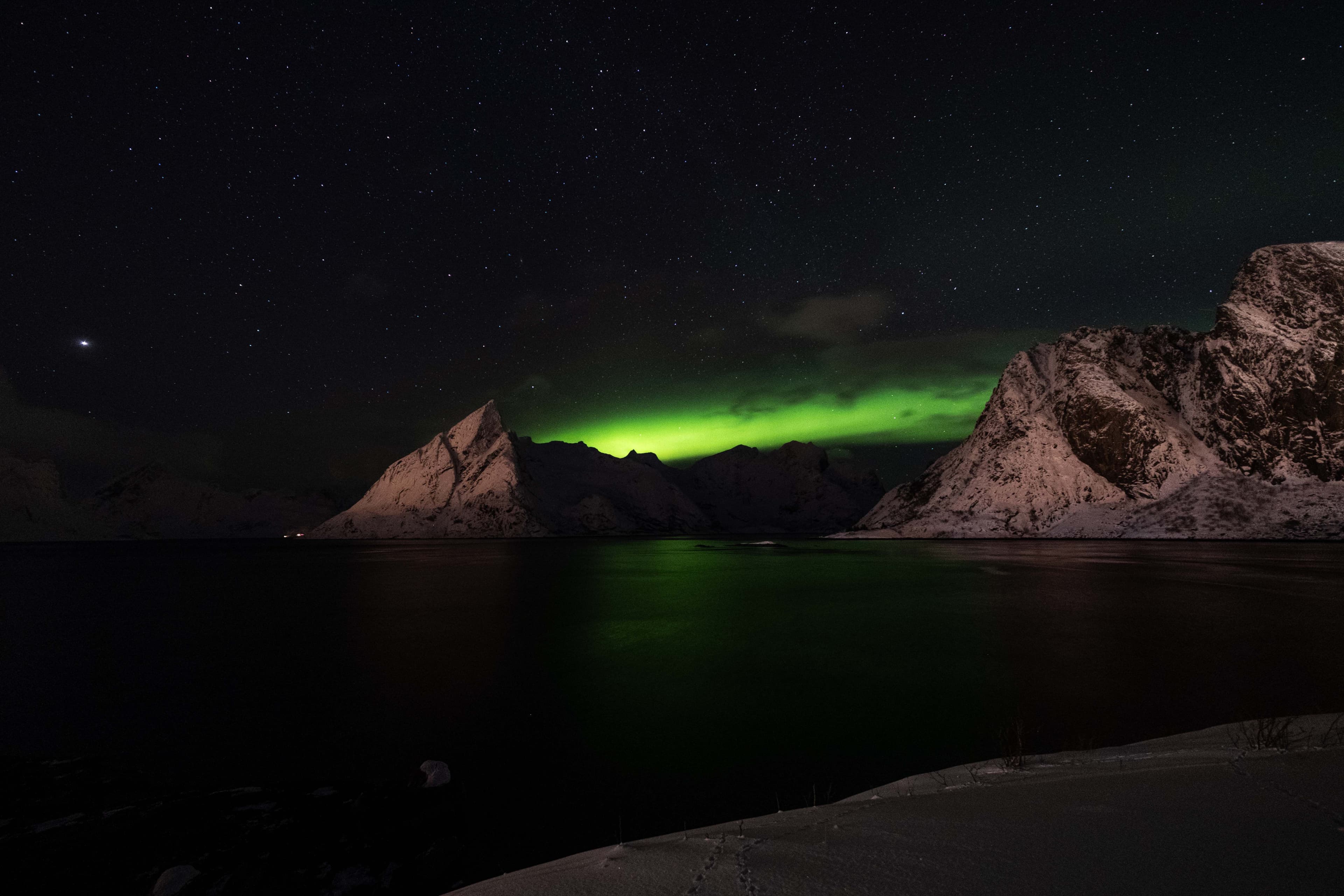 Aurora glowing above dark mountains and water in the Arctic night