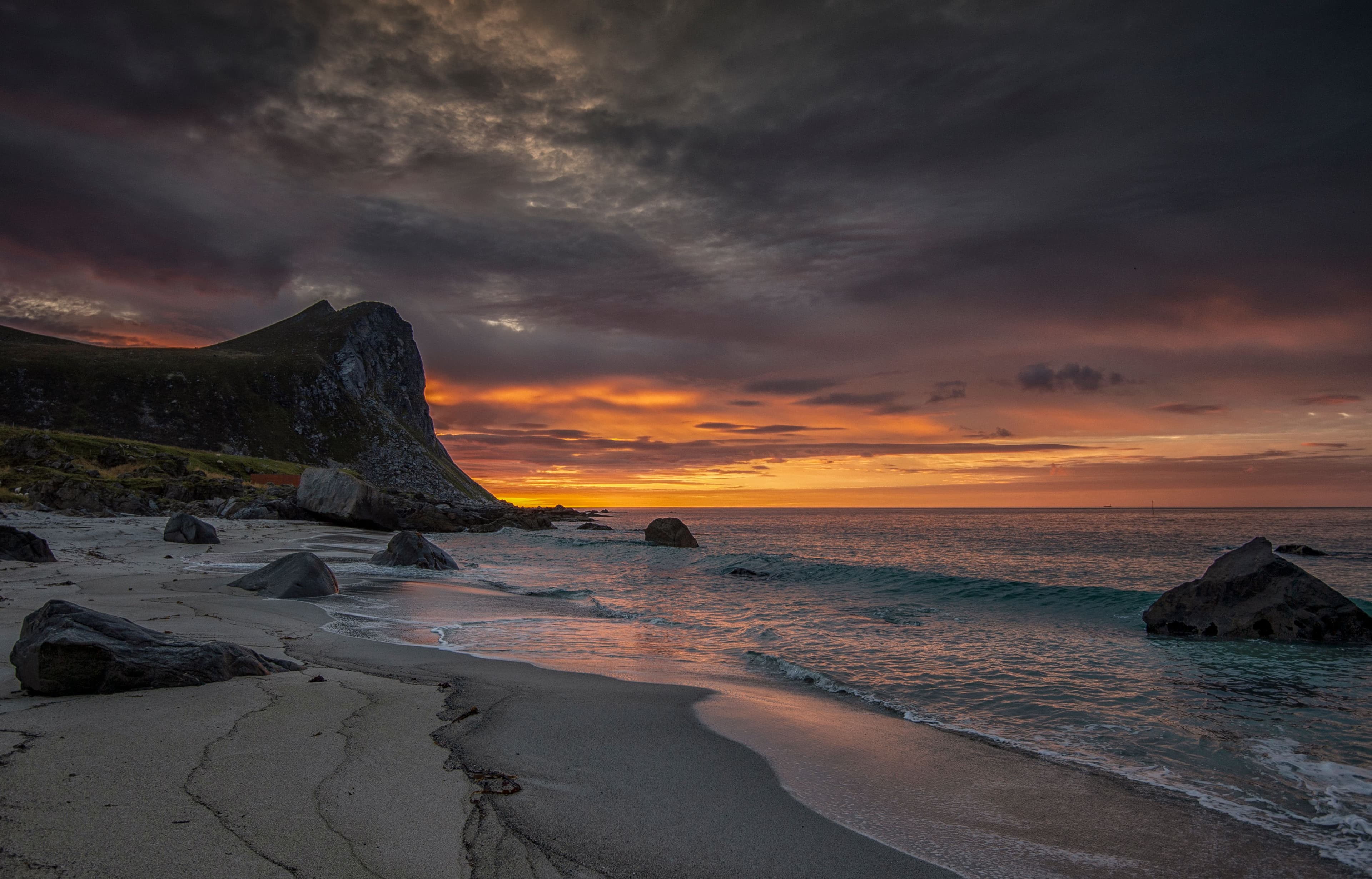 A dramatic Arctic beach with dark rock and a glowing sunset sky